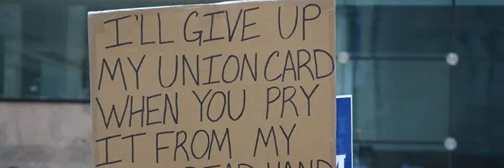 man holding sign in a crowd that says "i'll give up my union card when you pry it from my cold dead hand"