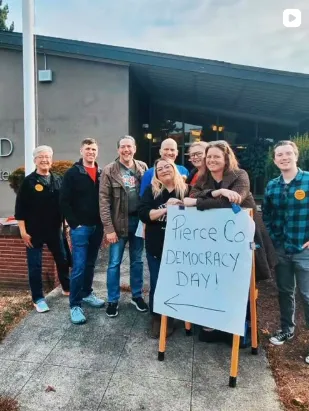 A group of PCCLC volunteers pose outside of the former Willard Elementary school around a sign that reads "Pierce Co. Democracy Day!"